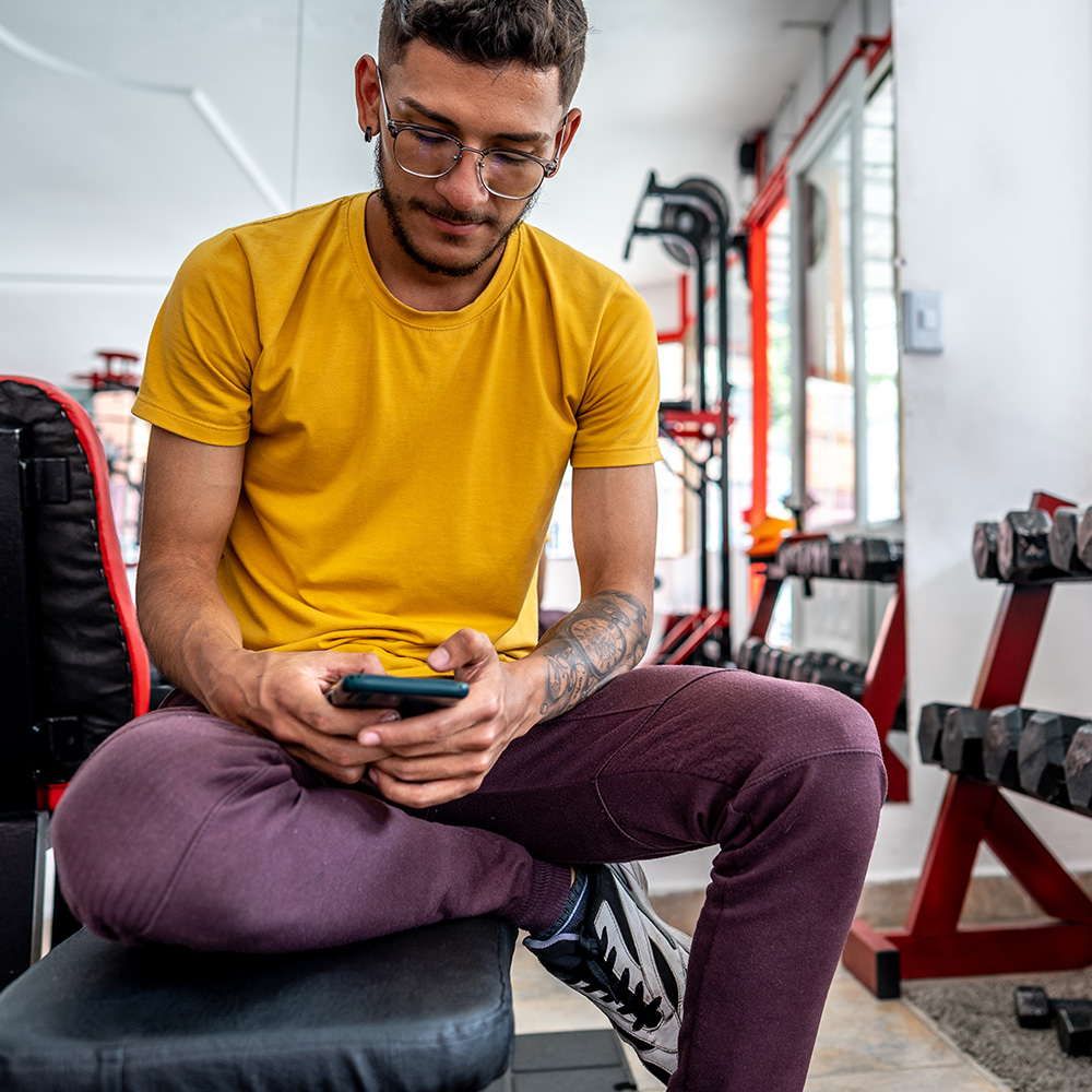 Man in yellow shirt sitting on gym apparatus texting on phone