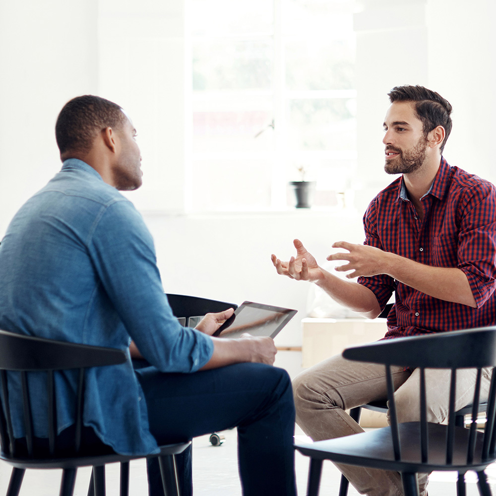 Two people talking while sitting in chairs facing each other in an office setting