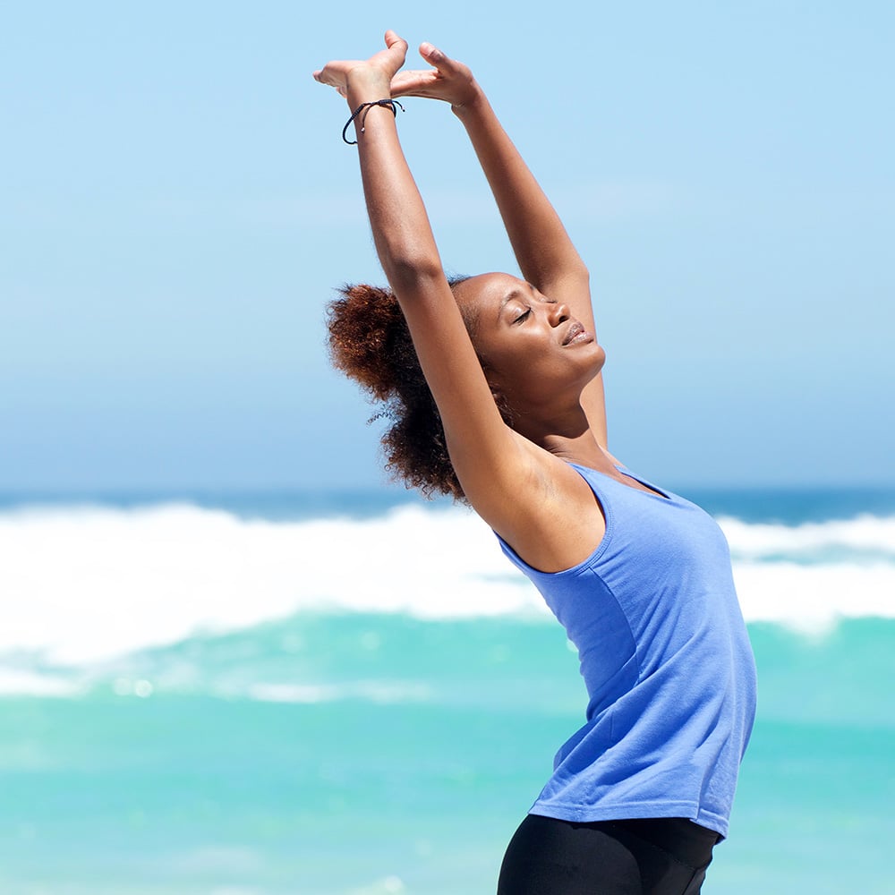 Woman in stretched yoga pose with aqua blue ocean waves in the background