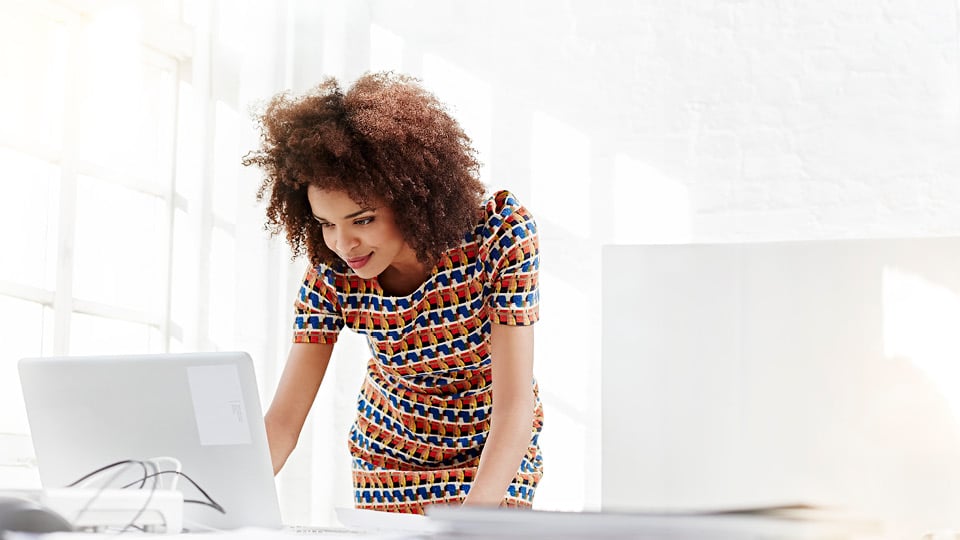 Woman in multicolored dress standing in white room leaning over white laptop