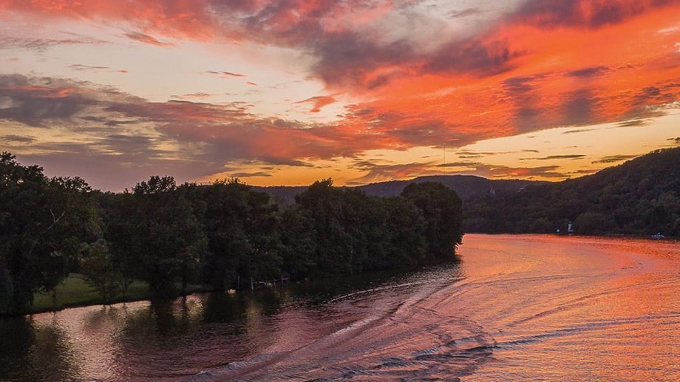 boat pulling waterskier on river at sunset with orange sky reflected on a water