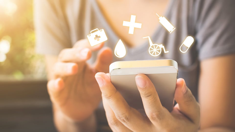 Close up of woman holding a cell phone with medical icons floating around the phone