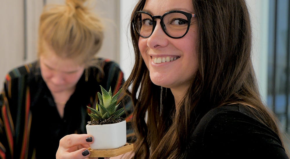 Close up of woman in dark framed glasses holding a small cactus in a white pot