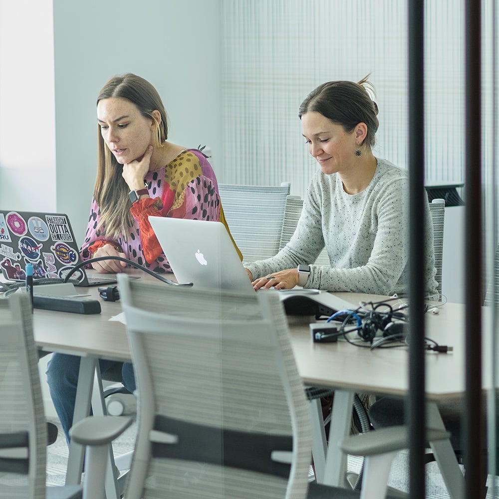 Two women sitting at conference room table on laptops