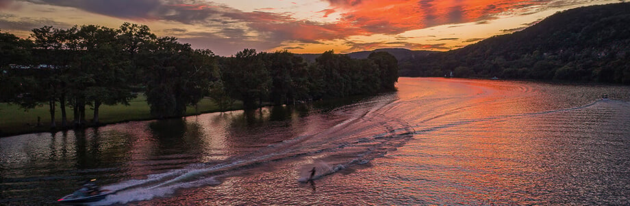 View of a water skiier on a river with sunset reflecting off the water at the bend in the river