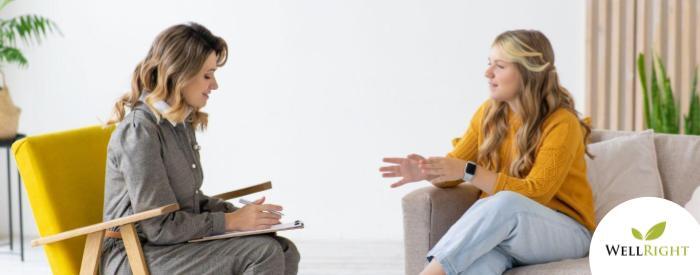 two women seated, facing each other, having a discussion. One is taking notes on a clipboard.