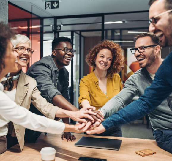 six people standing in conference room with hand stacked together in middle, ready to cheer