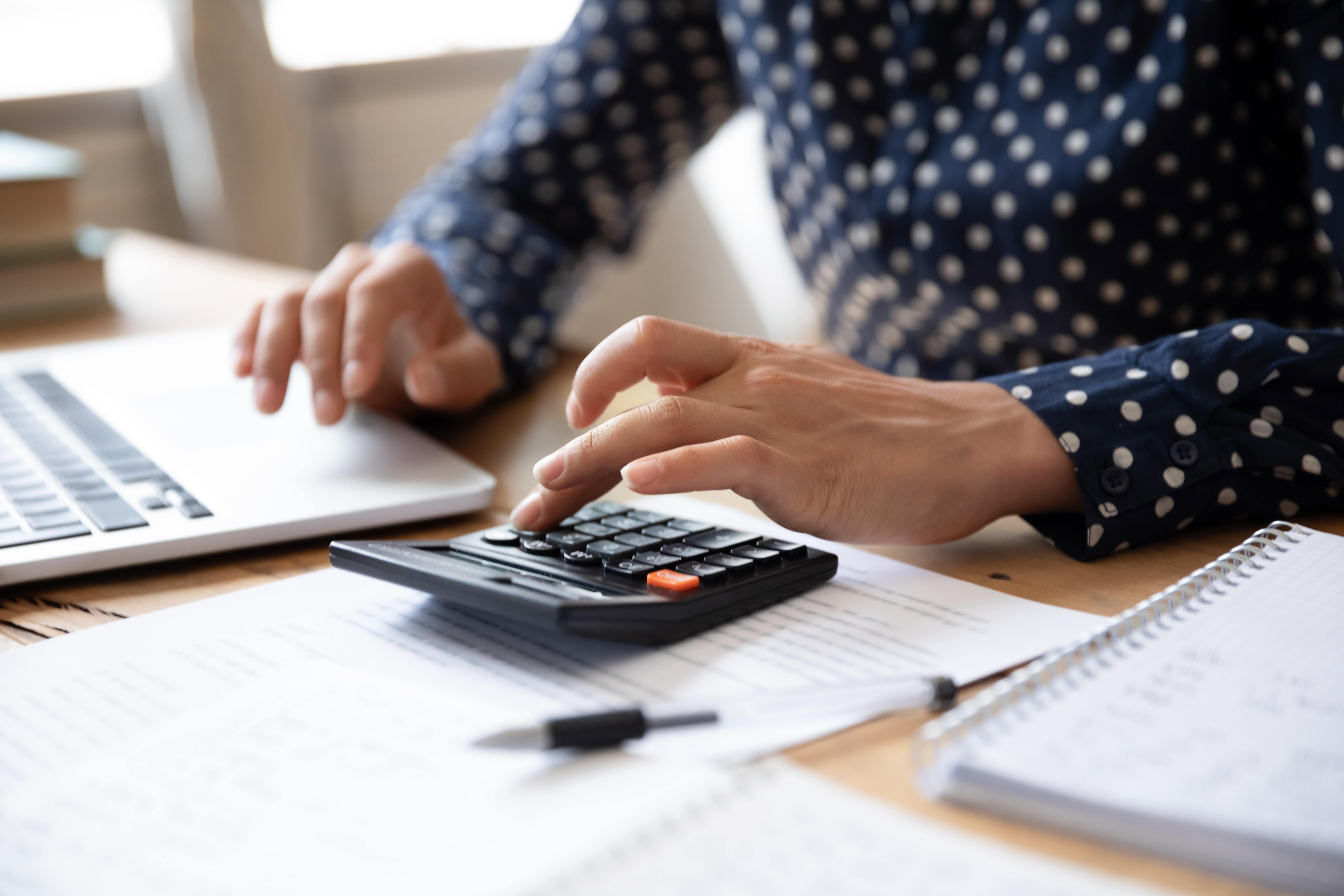 hands resting on a laptop and a calculator