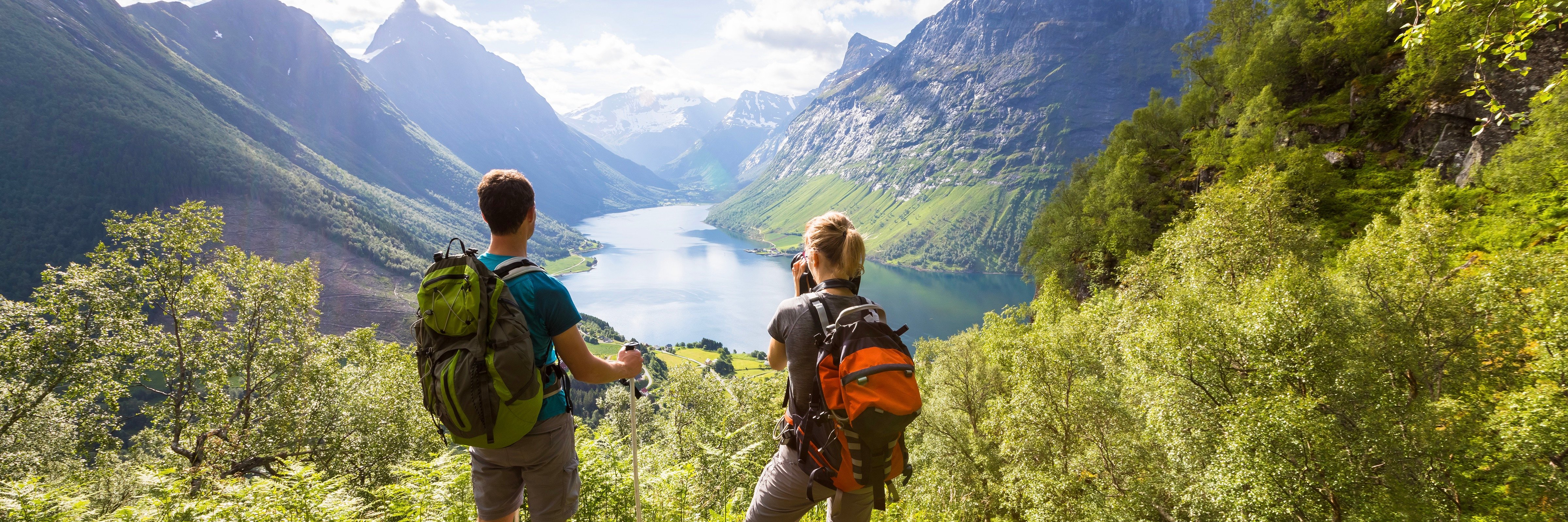 Two backpackers standing at the mouth of a valley, looking at a blue mountain lake
