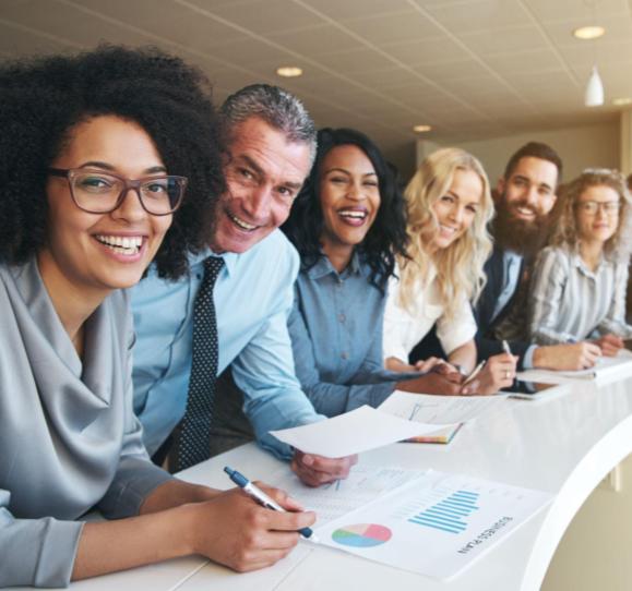 Six business professionals standing at a curved counter, smiling and looking at the camera