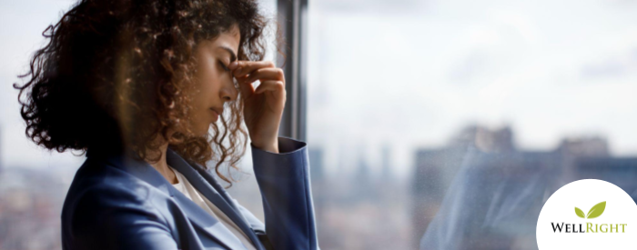 Stressed business woman standing at window while pinching the bridge of her nose